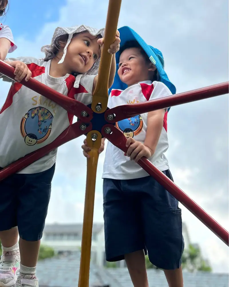 Two Shaws Preschool children grinning at each other from the top of an outdoor climbing frame in the early morning