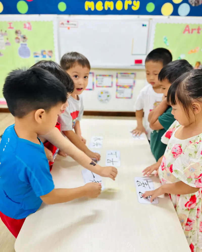 Preschoolers reaching across a table for word cards during a Letterland literacy game at Shaws