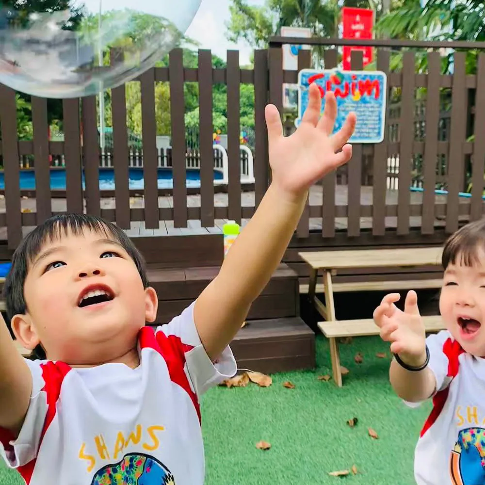 Two Shaws Preschool children stretching up to catch a soap bubble in the outdoor play garden