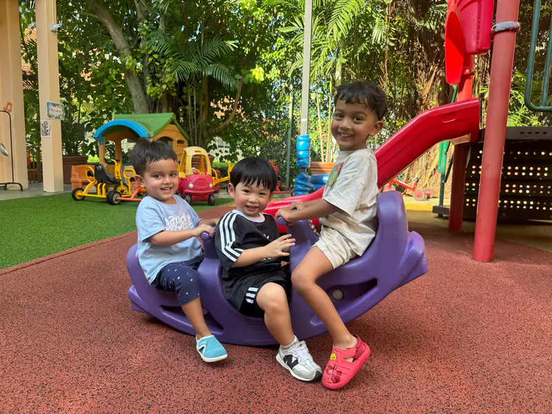Three preschoolers sharing a ride-on toy in a Shaws Preschool playground