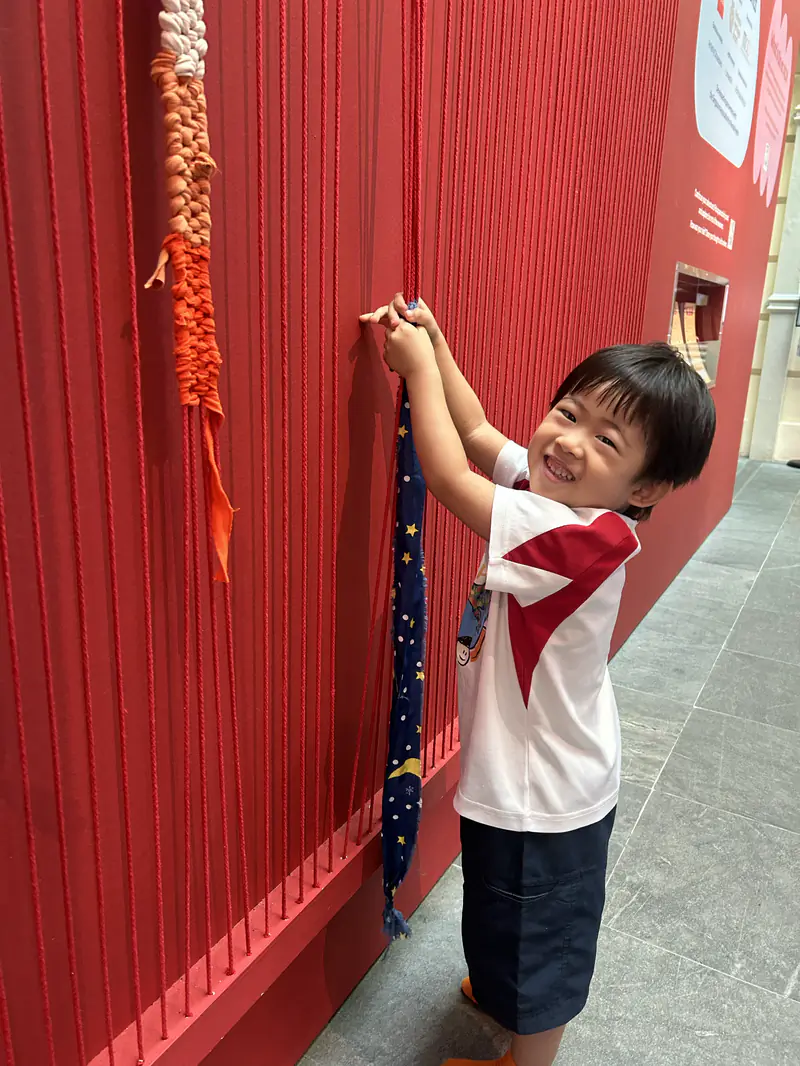 A Shaws Preschool girl reaching up to hang her own painting on the display wall