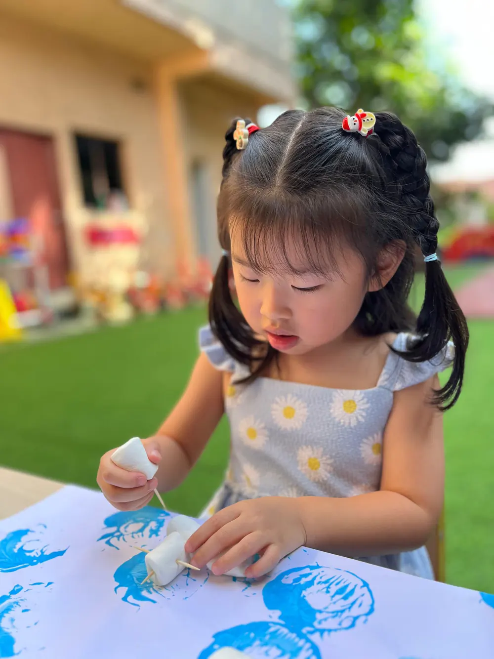 A Shaws Preschool girl concentrating on a block-printing activity at an outdoor table