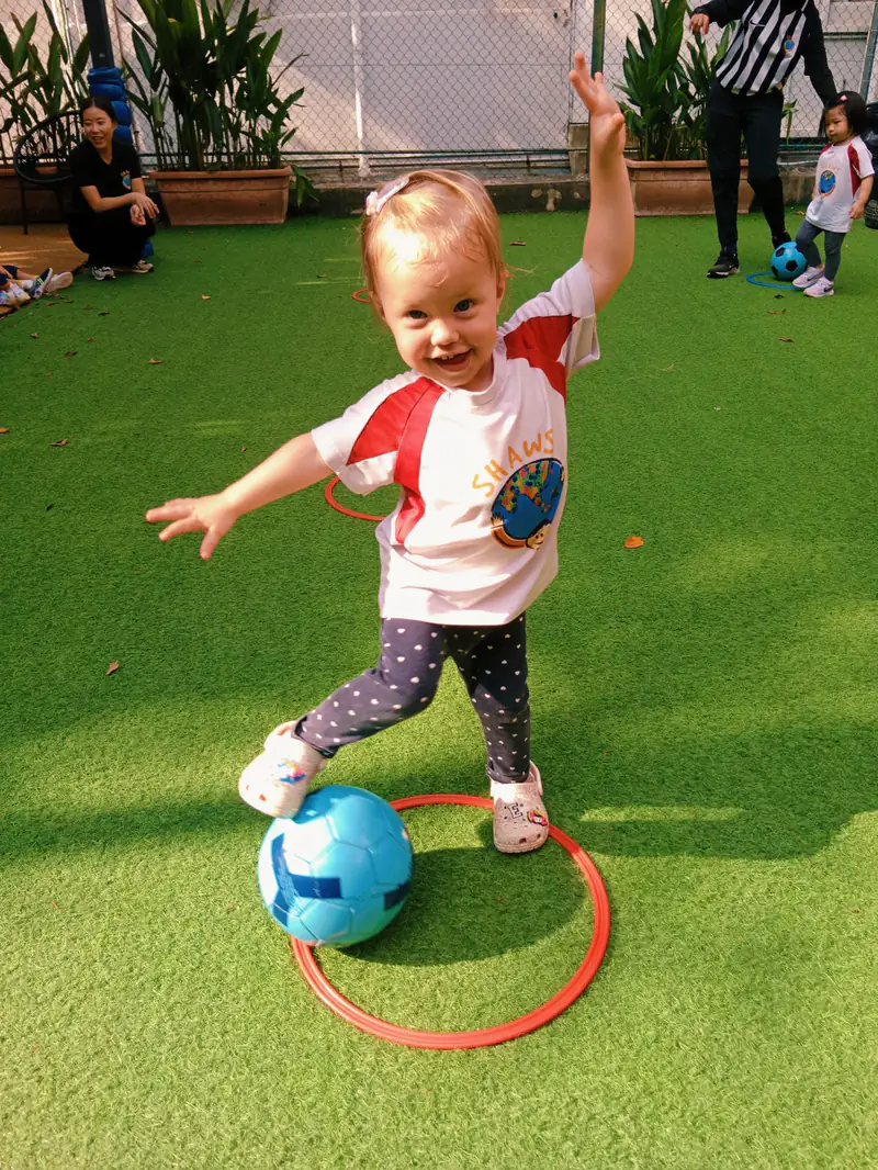 A Shaws toddler dribbling a football through a hoop during a Shaws Little League session