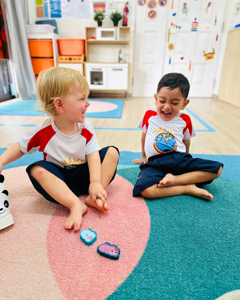 Two Shaws Preschool children sitting on the classroom carpet laughing together over a game